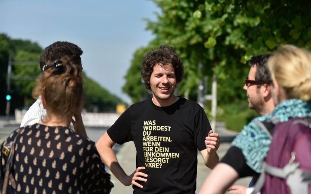 Happy young man in Berlin with T-Shirt saying: What would you do if your income were taken care of?